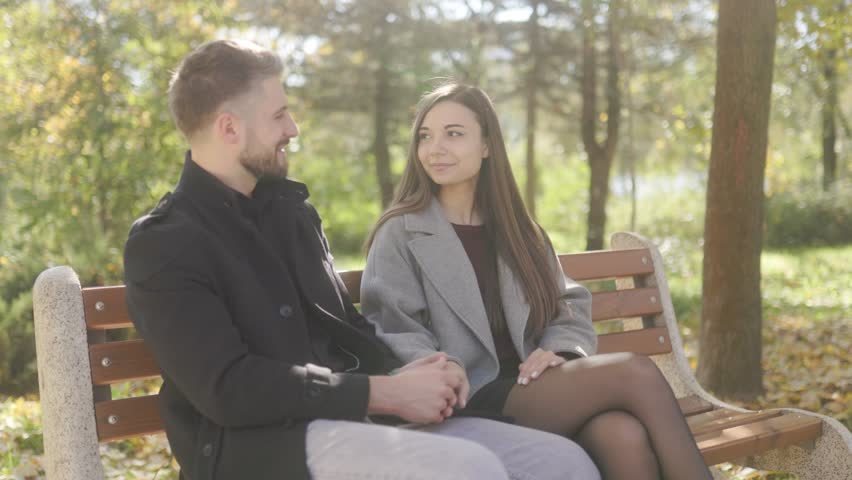 Surrounded by autumn leaves, a young couple shares a heartfelt embrace on a park bench. The natural setting enhances the intimacy of this romantic outdoor scene.
