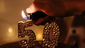 Happy Birthday Chocolate Cake with golden 50 Candles indoor with garland. A human hand lights candles using a lighter in a cozy home festive atmosphere. Close up view - Powered by Shutterstock - Get 15% off with code: PIKWIZARD15