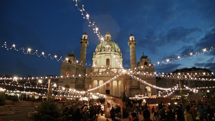 Karlsplatz Christmas Market in Vienna, Austria during evening. Christmas lights and decorations, happy people drinking tea and punch. Children playing. The church of Karlskirche in the background.