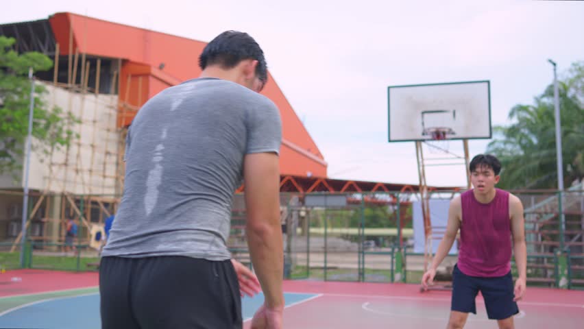 Asian two male player practice basketball shooting at outdoors court. Attractive sportsman people in sportswear exercise and workout by playing basketball game for health care activity at urban court.