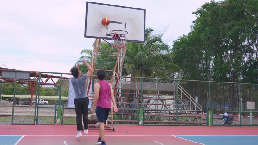 Asian two male player practice basketball shooting at outdoors court. Attractive sportsman people in sportswear exercise and workout by playing basketball game for health care activity at urban court.