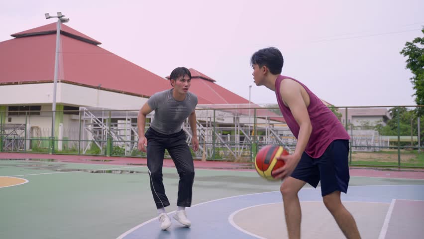 Asian two male player practice basketball shooting at outdoors court. Attractive sportsman people in sportswear exercise and workout by playing basketball game for health care activity at urban court.