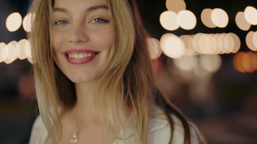A close-up of a happy woman smiling at night, with a beautiful bokeh background of lights. Happy Woman Smiling at Night with Beautiful Bokeh Background. Beautiful Woman Posing