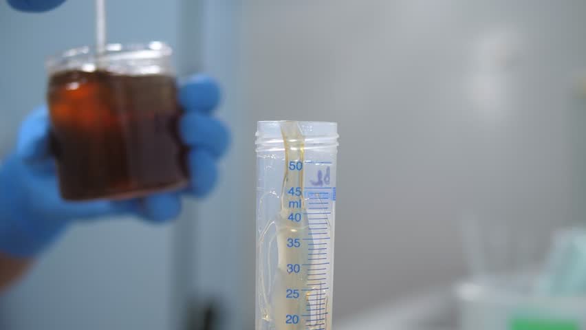 A close-up of a laboratory assistant pouring honey into a test tube with a scale in a laboratory at production. Checking the quality of natural honey.