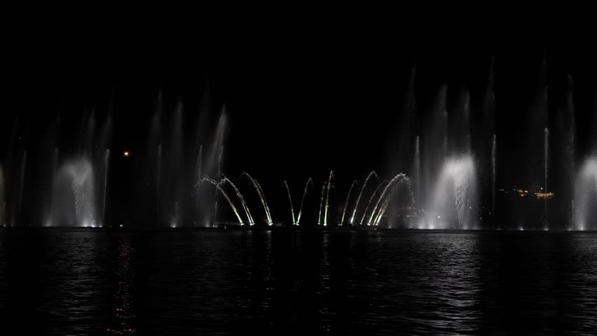 A beautiful singing fountain with colorful streams of water on a small lake. Illuminated water jets create a beautiful picture. Fountain show in the evening in the dark.