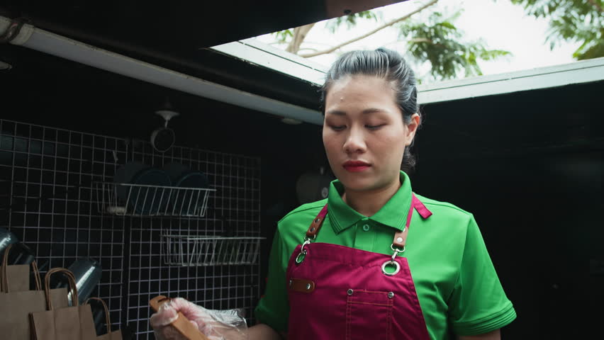 Tilt down shot of Asian woman in red apron cooking fried egg while working in food truck