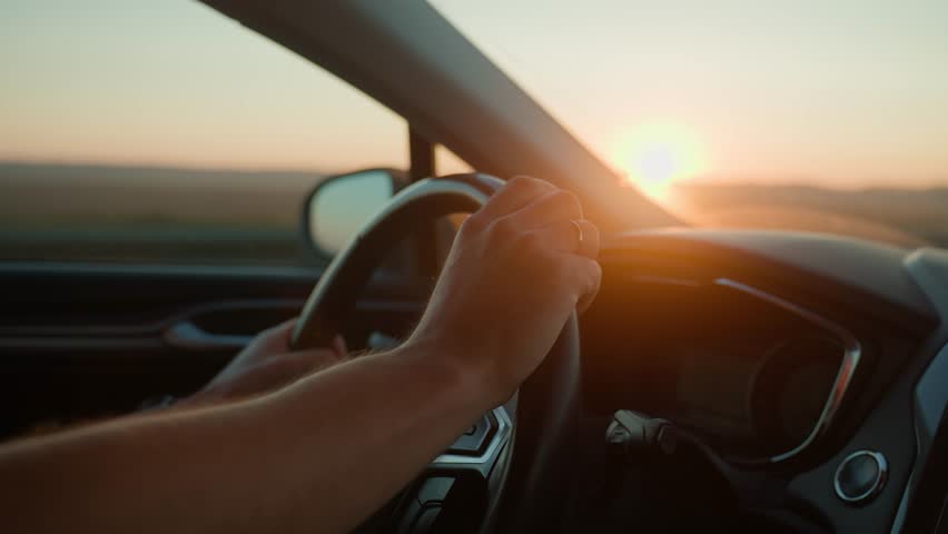 Male driver driving car, inside view. Man driving car on highway road at sunrise. Close-up of driver hands turning steering wheel