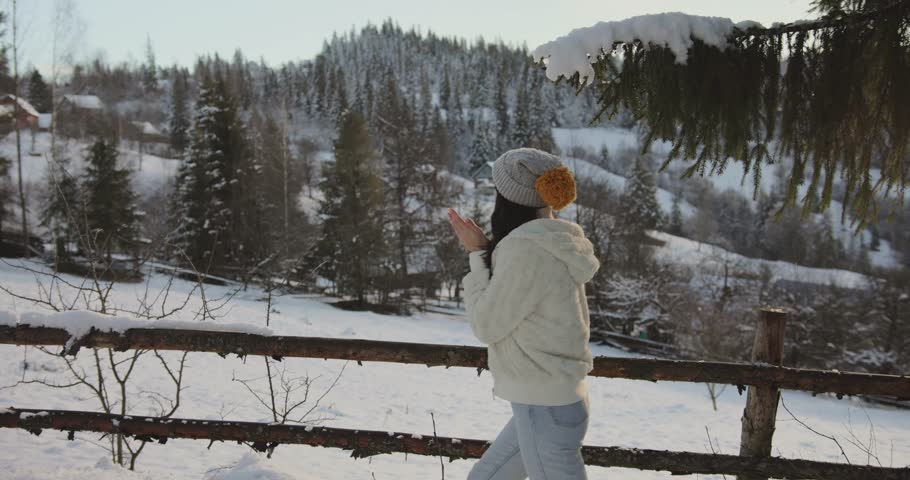 A young woman dressed in warm winter clothes walks along a snowy road in a peaceful mountain village, surrounded by trees and cottages. Perfect for lifestyle, travel, and winter themes. 