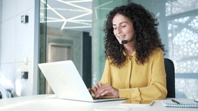 Young adult woman in wireless headset customer service representative operator talking on video call on laptop sitting in business office. Agent of the call center advises client, answering questions - Powered by Shutterstock - Get 15% off with code: PIKWIZARD15