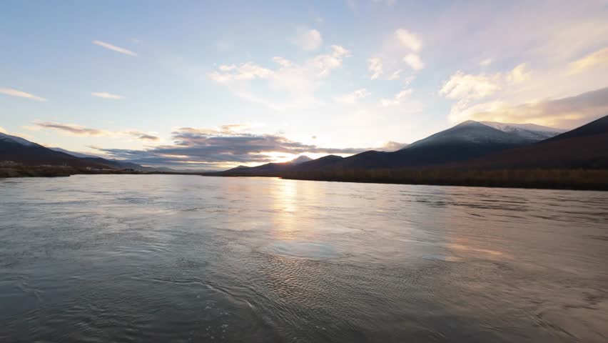 Immerse yourself in the breathtaking landscape of Yakutia as the sun sets over its calm rivers, illuminating the majestic mountains. Nature's tranquility shines in this enchanting moment.