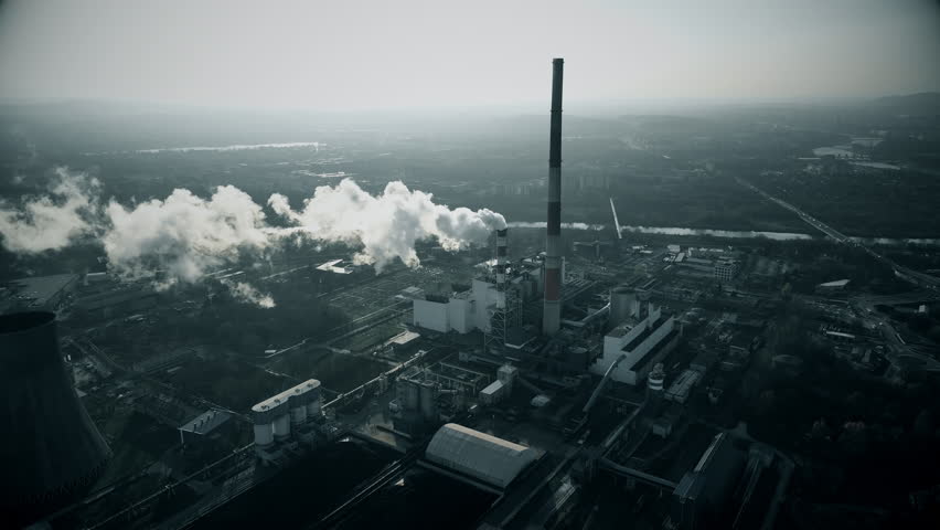 Industrial landscape reveals smokestacks releasing emissions into the atmosphere over a sprawling manufacturing site in a misty environment
