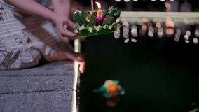 A hand gently releases a beautifully decorated krathong onto the water, its flickering candle and fragrant incense carrying wishes for good fortune during Loy Krathong in Thailand. - Powered by Shutterstock - Get 15% off with code: PIKWIZARD15