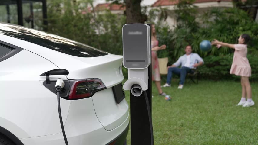 Electric vehicle recharge from home charging station on background of happy and playful family playing together. EV car using alternative and sustainable energy for better future Fastidious
