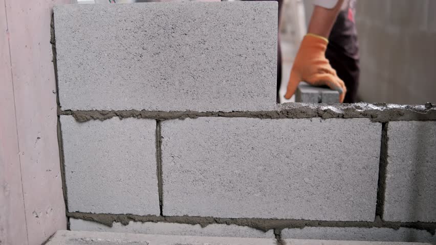 Construction worker laying concrete blocks, building wall, close up