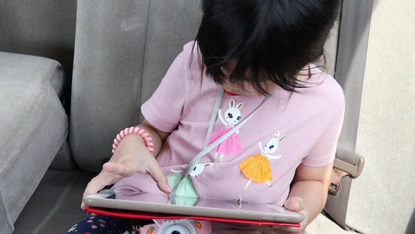 The cute Asian girl using tablet on the backseat of car.