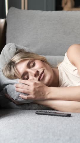Smiling young transgender woman in casual wear sleeping by remote control on sofa in living room at home