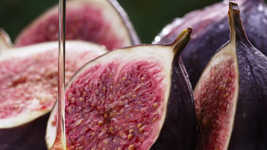 Sweet golden honey pouring on ripe figs slices. Healthy breakfast, natural dessert, juicy organic fig, exotic vegetarian food background. 