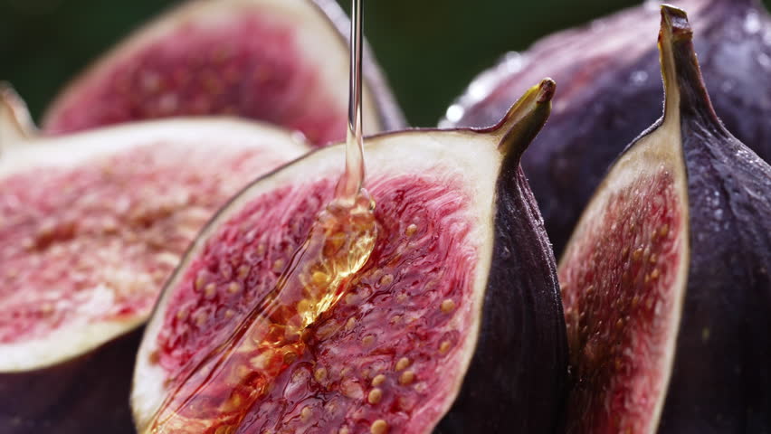 Sweet golden honey pouring on ripe figs slices. Healthy breakfast, natural dessert, juicy organic fig, exotic vegetarian food background. 