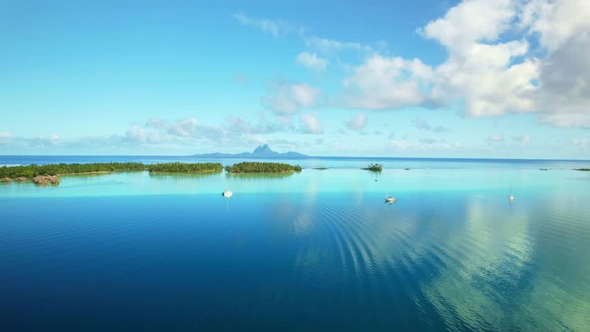 Drone Tahiti. Aerial view of Tahaa island lagoon, sailboat cruise in clear ocean water, Bora Bora island in background. Luxury honeymoon vacation getaway. tourism destination in French Polynesia