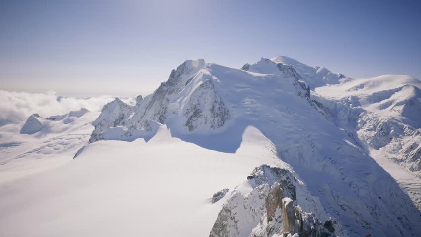 Mont Blanc stands majestically under a clear blue sky, bathed in sunlight, showcasing its snow-covered peaks and breathtaking alpine beauty.