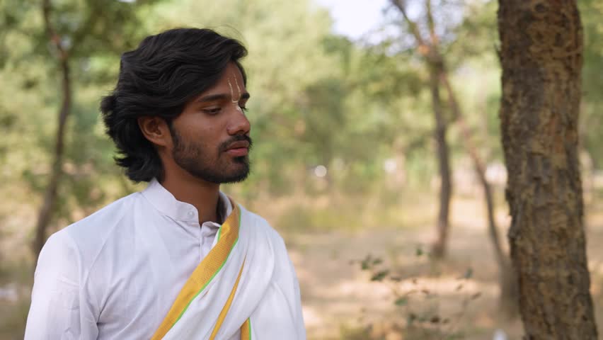 Young Indian athletic Hindu man wearing ramanandi tilak and traditional white dress exploring jungle.