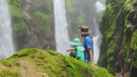 A father and his young son are joyfully admiring a stunning, breathtaking waterfall, which is beautifully surrounded by the vibrant and lush greenery typical of beautiful Costa Rica - Powered by Shutterstock - Get 15% off with code: PIKWIZARD15