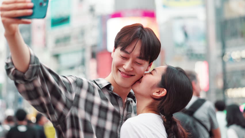 Happy, asian couple and selfie with kiss in city for memory or picture together in Tokyo. Japanese, man and woman with smile, affection or love for photography or moment in an urban town of Japan