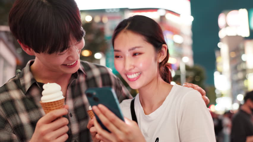 Bonding, night and couple with smartphone, city and smile for live stream, love and vlogger in holiday. Outdoor, eating and influencer with ice cream, fun and Japanese people on vacation and Tokyo