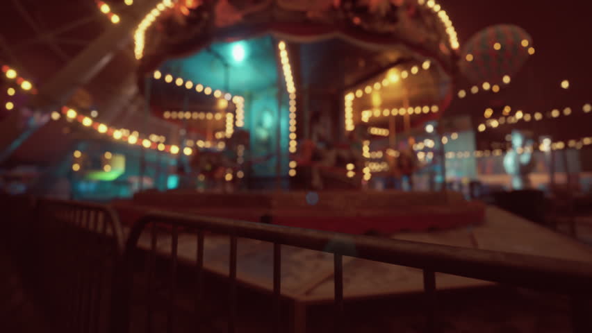 An amusement park lies quiet and still at night, featuring an empty carousel surrounded by glowing lights. The atmosphere feels eerie yet nostalgic, lacking the usual sounds of laughter and joy.