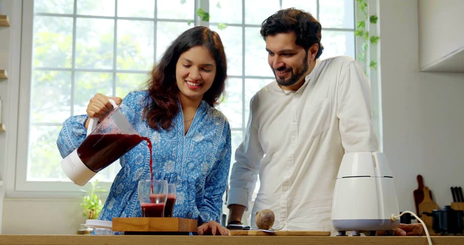 Indian young wife prepares fresh beetroot juice and serves it to her husband in the kitchen, highlighting health and nutrition for a wholesome lifestyle