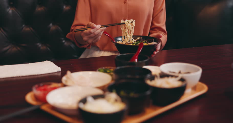 Eating, hands and ramen bowl in restaurant for nutrition, lunch and dinner meal with vegetables or noodles. Customer, person and food with chopsticks for healthy dish and traditional Japanese cuisine