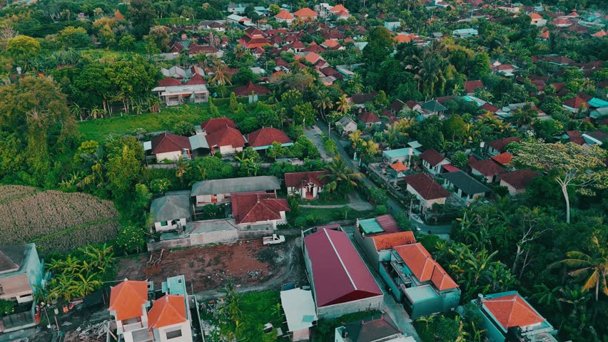 Aerial shot of a tropical rural landcape. The drone soars above a rural Balinese landscape, showcasing traditional houses nestled among lush greenery. Slow living concept.