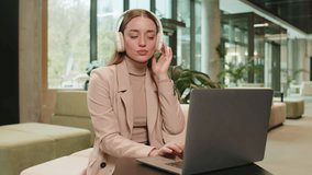 Happy relaxed overjoyed Caucasian young businesswoman girl in wireless headphones dancing listening relaxing music while working on laptop computer in modern office lobby. Lady sitting in hotel hall - Powered by Shutterstock - Get 15% off with code: PIKWIZARD15
