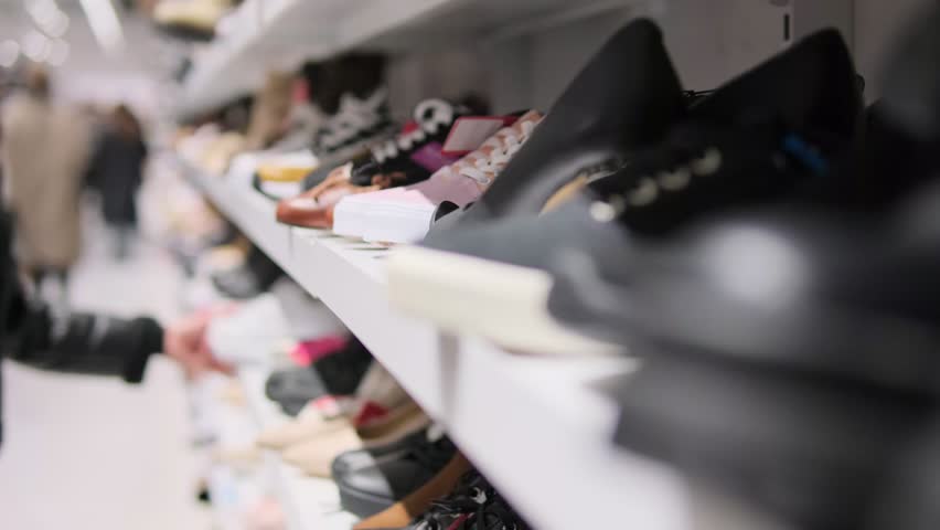 Shoes on a retail shelf with blurred shoppers in the background.