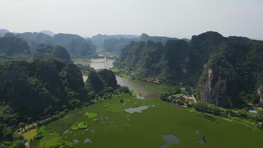 Drone shot of beautiful green water-fern lake between jungle covered limestone mountain in Ninh Binh Viet Nam