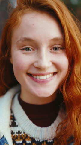 Horizontal portrait face attractive young woman with red hair looking at camera smiling. Stand in forest at sunlight. Slow motion