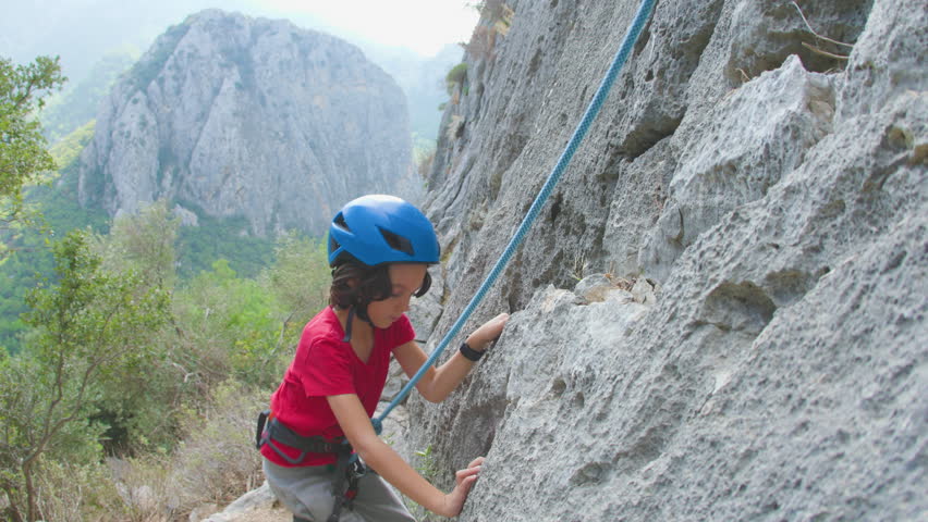 Children's rock climber. A boy in a helmet climbs a rock. A child is rock climbing in a natural area. A sporty kid spends his time actively. Play sports outdoors.