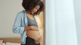 Portrait of Black African American Pregnant woman in curly hair standing embrace her belly at home. Expecting mother. Pregnancy concept. - Powered by Shutterstock - Get 15% off with code: PIKWIZARD15