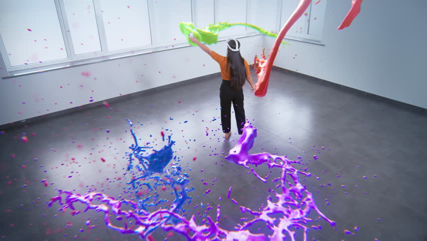 Talented Asian young woman wearing VR headset paints with wireless controllers, uses gestures to create abstract online artwork. Holographic 3D rendering of paint drops. Augmented reality technology.