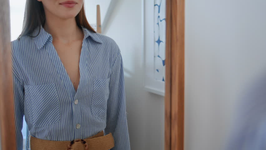 Young lady looking mirror trying clothes at wardrobe closeup. Happy woman choosing outfit before party. Joyful girl enjoy new purchase staring reflection. Smiling student holding hanger with dress 