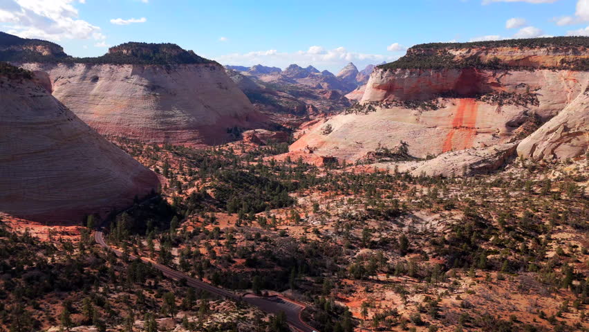 Aerial drone shot captures the vibrant landscapes of Zion National Park, showcasing magnificent red rock formations illuminated by a stunning sunset, enhancing their natural beauty