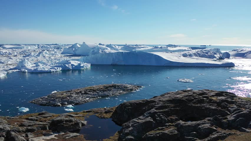 Explore stunning ice formations along the coastline of Greenland, showcasing the beauty and intricacies of natural ice structures reflecting in the surrounding water under a clear sky.