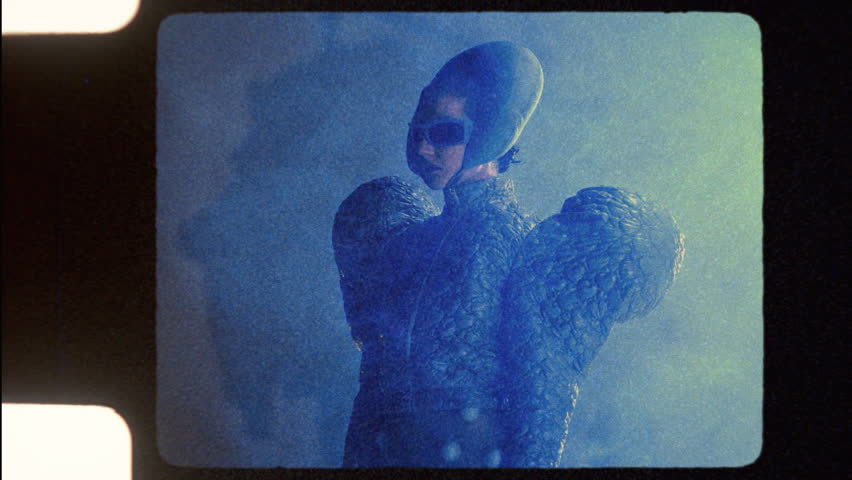 An avant-garde artist in a striking blue costume and stylish shades walks through a mist-filled studio, creating an ethereal atmosphere that enhances the boldness of their unique ensemble