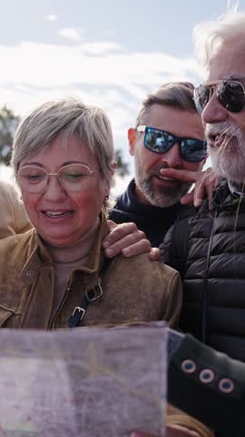 Vertical group diverse middle-aged tourist people standing looking at travel map in hands on street vacation joyful searching interest city places. Adults friends in community enjoying trip together 