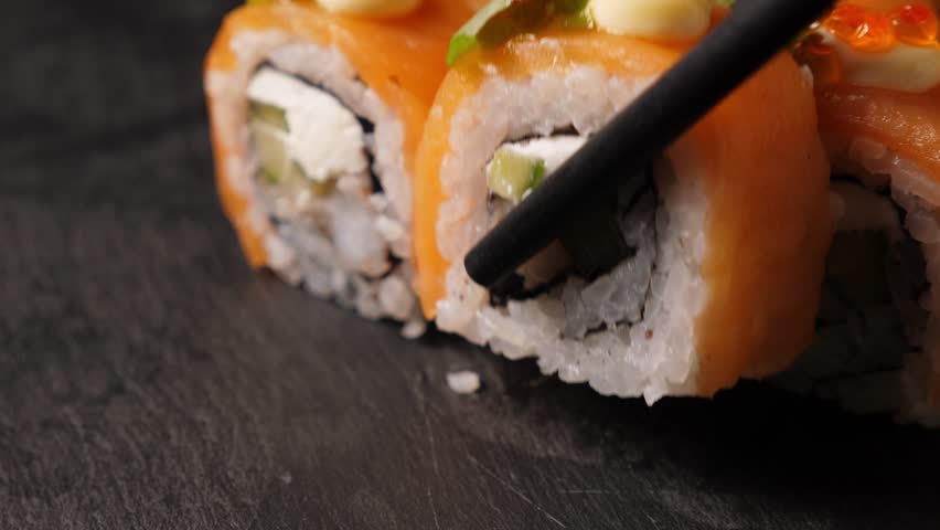 Take one sushi roll from black slate platter using chopsticks, Closeup