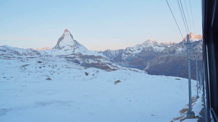 Gornergrat bahn railway running towards summit station with Matterhorn mountain peak background in Zermatt on a sunny winter day. Swiss Alps, Switzerland travel journey trip Shot from train window.