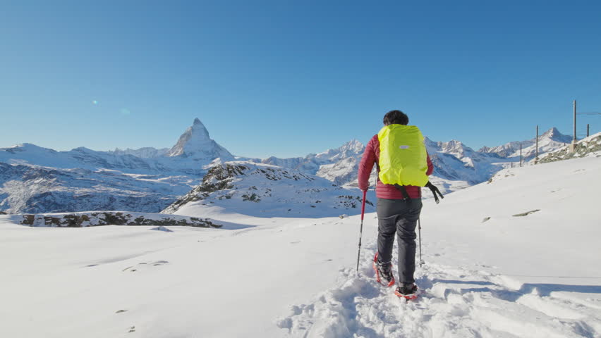 Asian man tourist hiker with backpack walking in snow shoes with famous Matterhorn background. Adventure climber hiking up to swiss alps mountain top. Switzerland travel lifestyle winter activities. - Powered by Shutterstock - Get 15% off with code: PIKWIZARD15