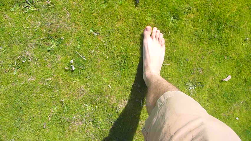 Point of view of man walking barefoot through grass field.