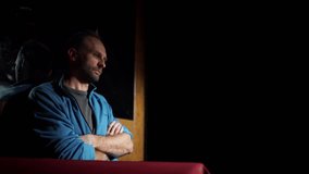 A middle-aged man sitting indoors, resting his head on his hand, with a thoughtful expression. The dimly lit room has a calm atmosphere, and blinds partially cover the window behind him - Powered by Shutterstock - Get 15% off with code: PIKWIZARD15