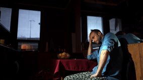 A middle-aged man sitting indoors, resting his head on his hand, with a thoughtful expression. The dimly lit room has a calm atmosphere, and blinds partially cover the window behind him - Powered by Shutterstock - Get 15% off with code: PIKWIZARD15